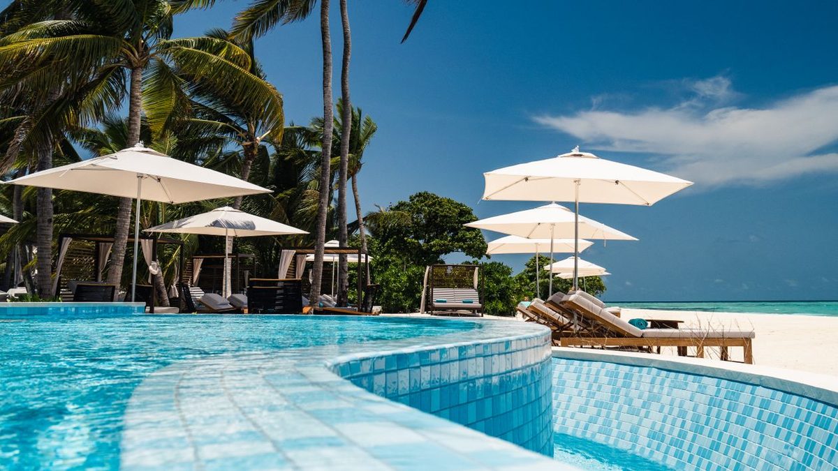 A resort pool edged with palms above a white-sand beach