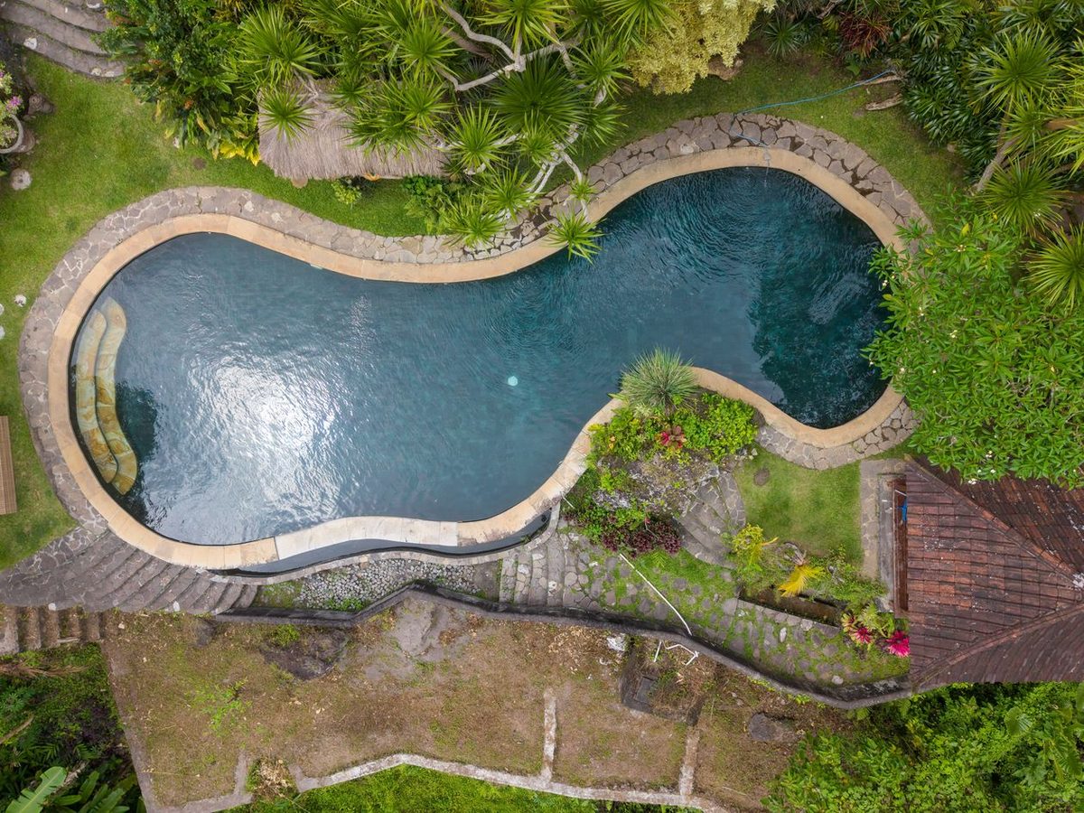 A private villa pool seen from above, ringed by gardens