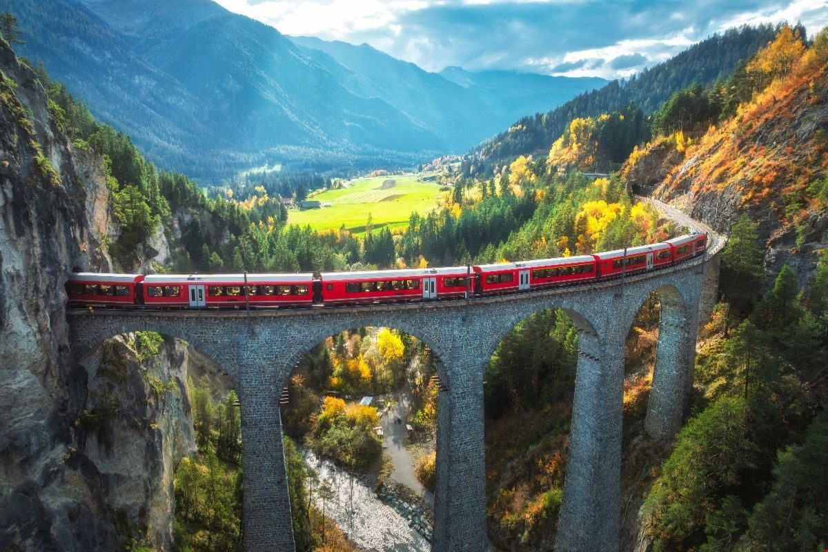 A red scenic train crossing a stone viaduct in the Alps — Italy by rail